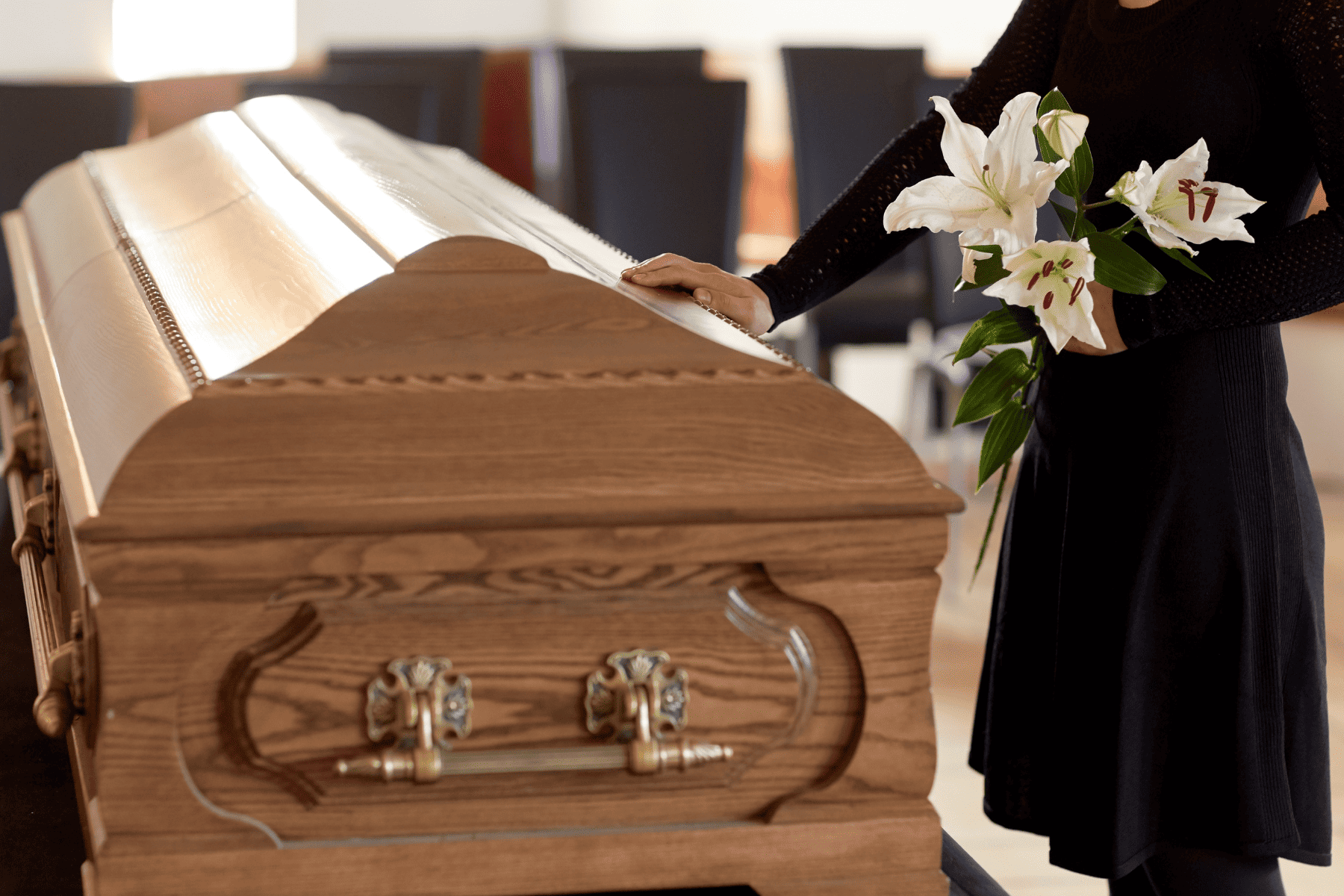 A woman dressed in black with her hand resting on the top of a funeral casket